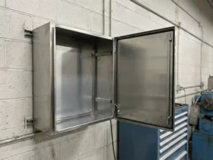 Geöffneter wandmontierter Stahlschrank mit gebürstetem Metallinneren an grauer Industriewand, leer und neuwertig.